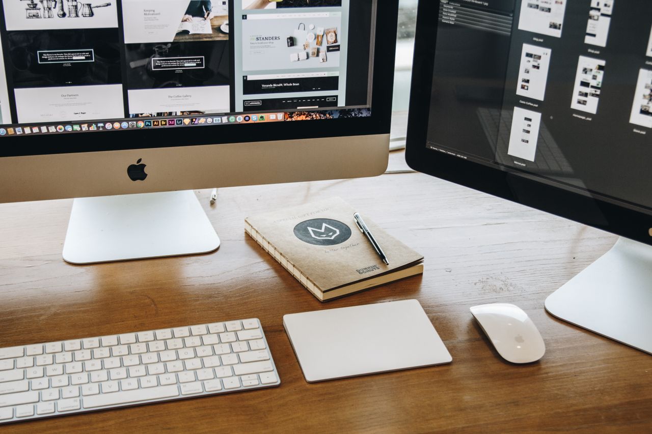 A minimalist desk setup with dual monitors, a keyboard, mouse, and notebook, designed for productivity.
